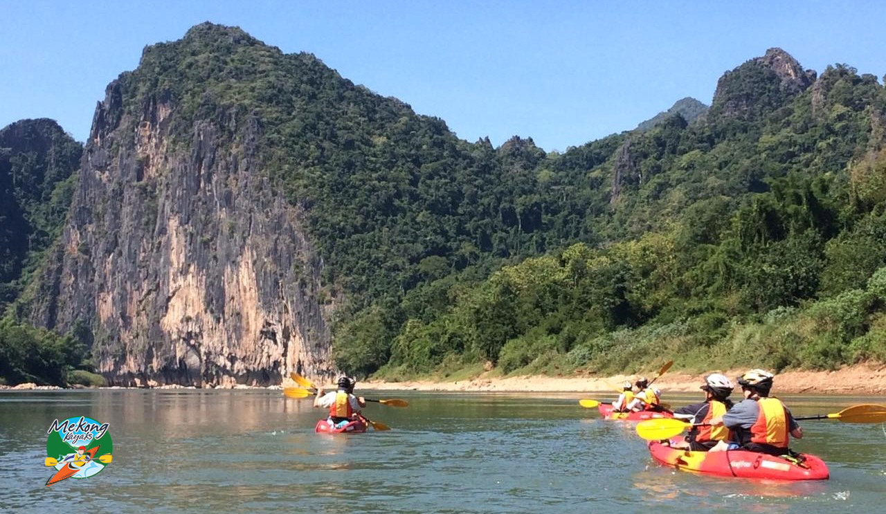 Kayakers on the Nam Ou River approaching the 330m towering Pha Hung karst cliff
